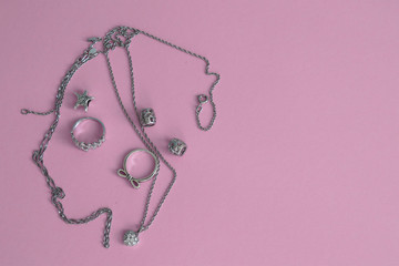 Photo of silver jewelry on a pink background. Ring, chain, beads, charms