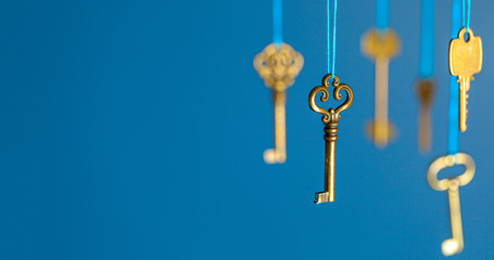 Many old keys of yellow gold color are hanging on thread on a blue background. The concept of the selection of access or password to the secret data. Copy space for text.