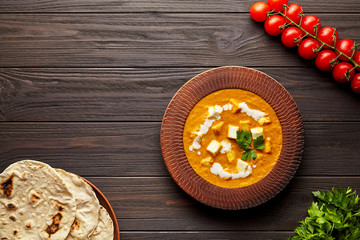 Shahi paneer traditional Indian vegetarian masala meal with vegetables and butter panir cheese spicy food vegan north India dish served with chapati, tomatoes and parsley on dark wooden background 