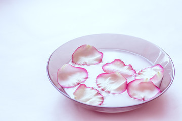 Rose petals in milk. Milk with petals in a plate.