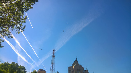 Traces of the aircraft and the silhouettes of the aircraft over the city in the blue spring sky.