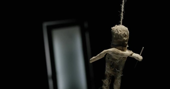 Silhouette of a man with a knife on the background of a voodoo doll. Play of light. Focus on the silhouette and on the doll.