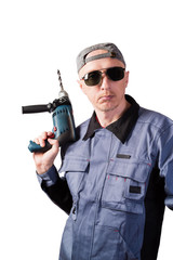 A man in working clothes, dark goggles and a cap, with an electric drill. A man of middle age, European appearance, in a working overalls. Isolated on white background