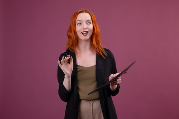 cute redhead caucasian woman stands on pink background holding her red cell phone and document folder