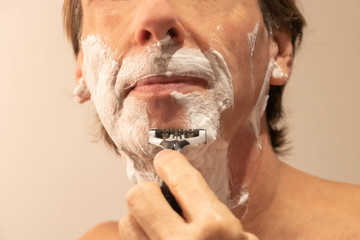 Homme de face, se rasant la barbe avec de la mousse à raser et un rasoir manuel