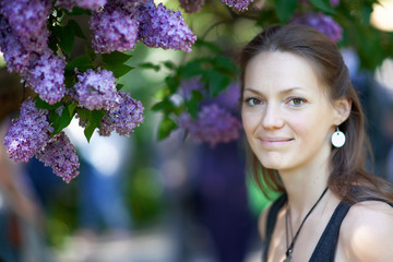 Beautiful young woman enjoying the smell of lilac in blossom garden in sunny spring day. Pretty female and flowers. Aromatherapy and springtime concept