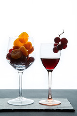Dried apricots and grape berries in glass and portion of red wine on white background