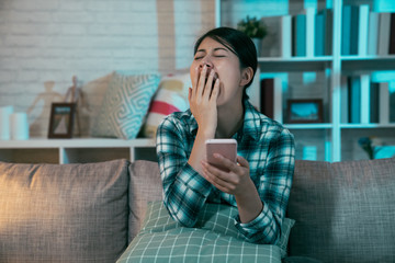 young beautiful asian woman on couch late at night texting using mobile phone sleepy and tired in...