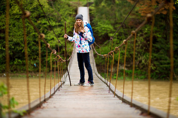 traveller woman with backpack walking in forest Crossing River by hinged bridge