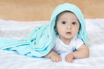 6-8-month-old baby boy lying playfully in bed. Charming 6-7 month little baby in white bodysuit. Baby boy in white bedding. Copy space