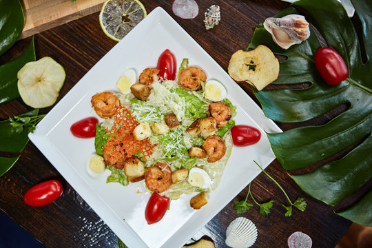 A shrimp caesar salad on a white plate surrounded by dried fruits and plant leaves - closeup photo