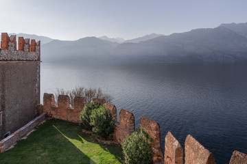 Fototapeta na wymiar The medieval Scaliger Castle (Il Castello Scaligero di Malcesine) and the view of the Alps in the fog from Lake Garda in Malcesine, Italy