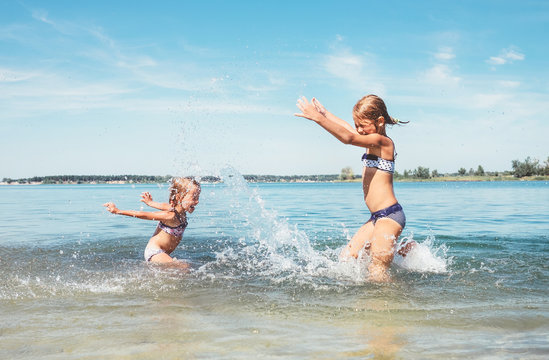 Two little sister girls fooling around in the calm sea waves splashing water to each other. Family vacation concept image.