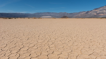 View of the arid soil with cracks in the desert of the Death Valley with mountains and blue sky on the background 