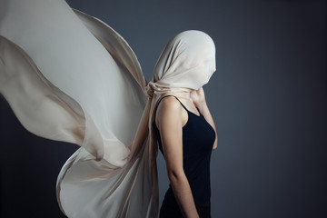An anonymous model, is covered by a beige veil. A woman in a black top with her head wrapped in a...