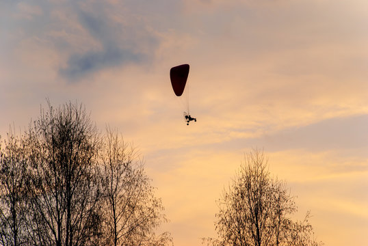 aeroshyut paragliding flying against the backdrop of the setting sun. A paramotor in the background sun