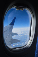 Airplane window view on the clouds and blue sky horizon. Plane wing vertical view in porthole