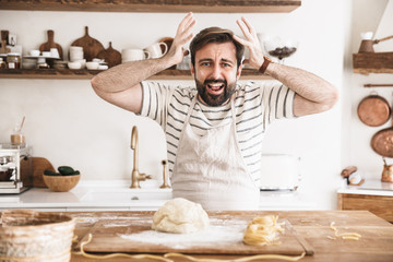 Portrait of nervous brunette man making homemade pasta of dough in kitchen at home