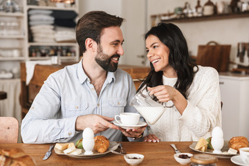 Portrait of cheery european couple drinking coffee while having breakfast in kitchen at home