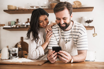 Portrait of joyful couple reading recipe while cooking pastry with flour and eggs in kitchen at home
