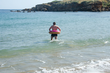 Fototapeta na wymiar Man with donut ring float inflatable swimming in Mediterranean Sea