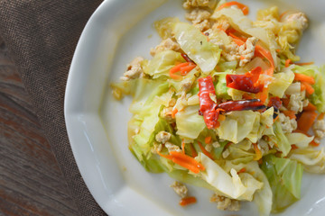 Top view stir fried cabbage  with mince chicken breast, red dried chili, slice carrots on white dish on wooden table for served with rice. Thai delicious food for dinner.