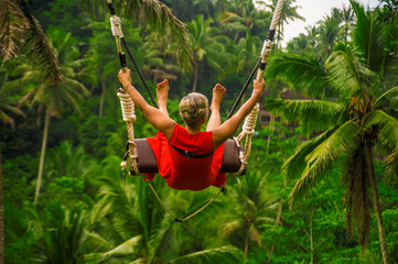  back portrait of attractive happy middle aged woman with grey hair riding rainforest swing...