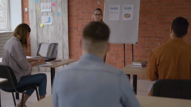 the teacher discusses topics from the textbook for the lecture with the students. the teacher walks between the rows of tables 4K