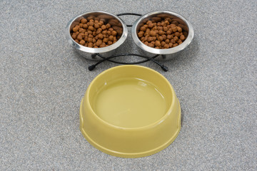 Obraz na płótnie Canvas Cat food in two bowls and water on a gray floor top view