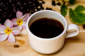 Black coffee cup with a pink frangipani flowers And green leaves And coffee beans are in the composition