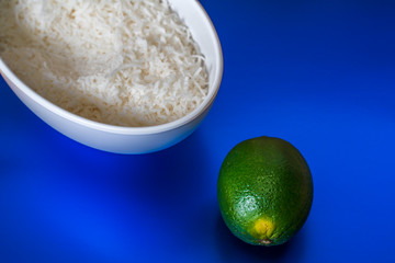 Lime and bowl of coconut flakes on a blue background.