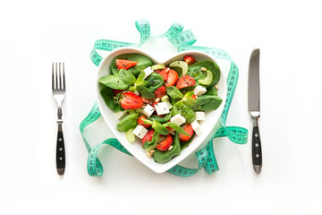 Fresh salad of strawberry, celery, spinach, cheese in plate as heart on white. Concept weight loss...