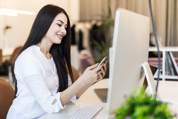Smiling young beautiful woman working at her smartphone and holds a hand near the head in the modern spacious office