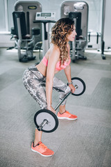 Attractive muscular fitness woman raising weight in the gym