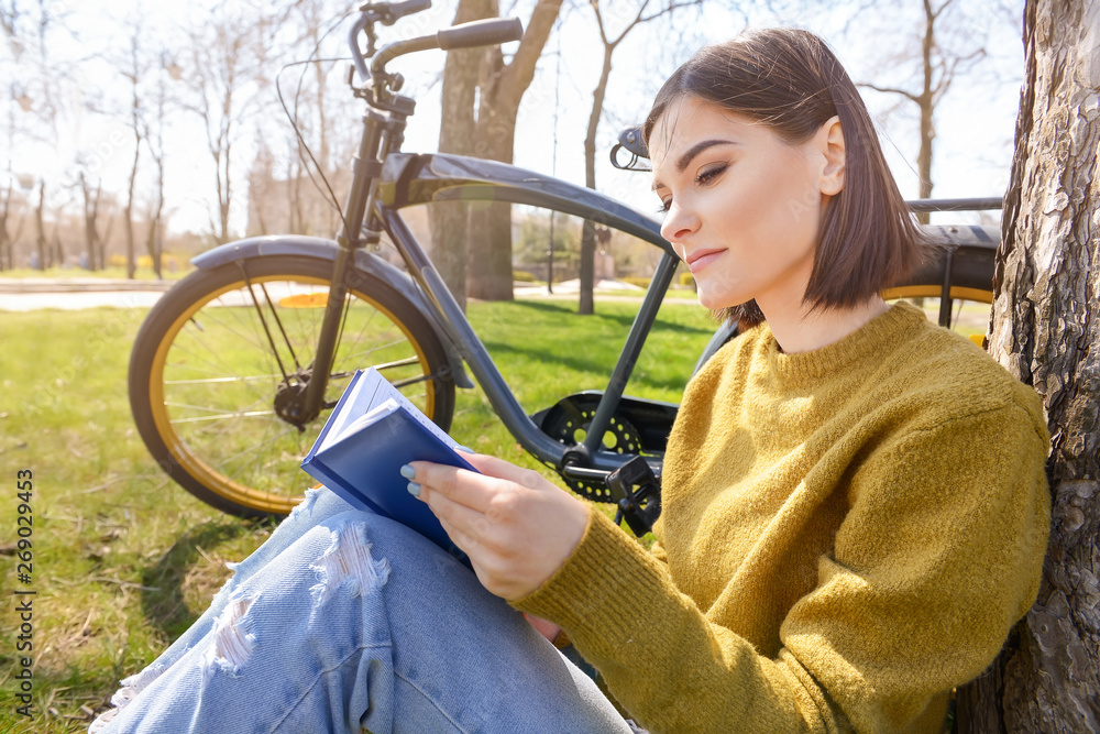 Wall mural Beautiful young woman reading book in park on spring day