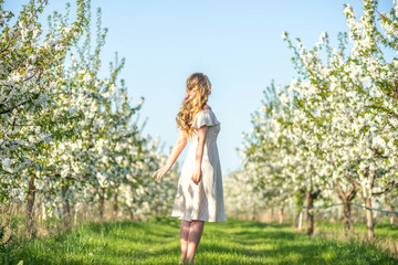 Woman in a blooming orchard at springtime. Enjoying sunny warm day. Retro style dress. Colorful spring moods