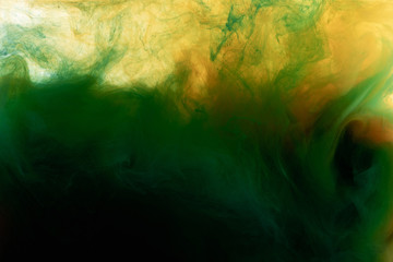 Close up view of dark green and orange paint mixing in water