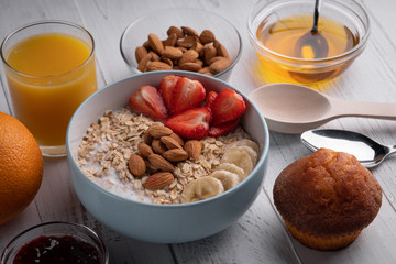 Healthy breakfast: oatmeal porridge with fresh strawberry, banana and nuts. Overhead view. Muffin. Juice. Honey