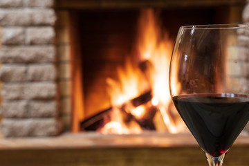 Glass of wine against cozy burning fireplace background, christmas evening.