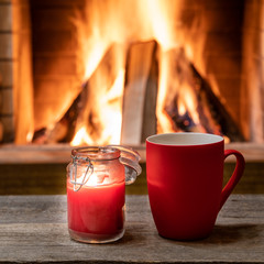 Red mug with hot tea, and a candle ,near cozy fireplace, hygge, home sweet home.