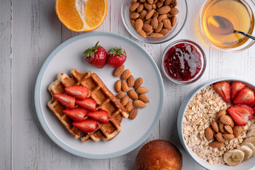 Colorful and tasty breakfast ingredients on white table Homemade oatmeal, waffles, fresh juice,...