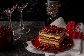 sweet, tempting tiramisu, sprinkled with red grains of pomegranate, on a black stone table, next to it red wine in crystal glasses