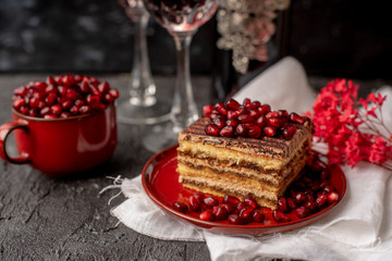 sweet, tempting tiramisu, sprinkled with red grains of pomegranate, on a black stone table, next to it red wine in crystal glasses