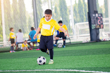 blurry ball with Asian kid soccer player speed run to shoot ball to goal on artificial turf.