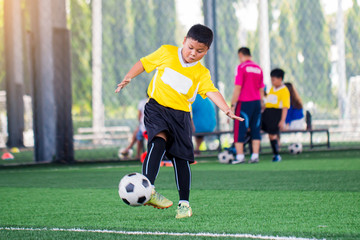 blurry ball with Asian kid soccer player speed run to shoot ball to goal on artificial turf.