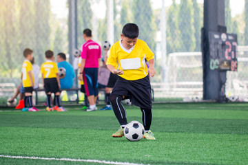 blurry ball with Asian kid soccer player speed run to shoot ball to goal on artificial turf.