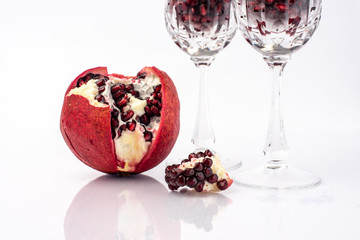 on a white background, isolated, blood-red, pomegranate fruit next to a crystal glass, filled to...