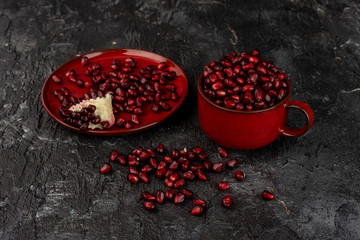 on a black, stone background, bloody red pomegranate seeds in a red cup and on a red plate