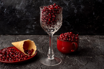 on a black, stone background, bloody red pomegranate seeds in a red cup and on a red plate