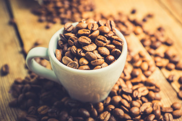 Coffee beans in white cup on the rustic wooden background. Selective focus. Shallow depth of field.